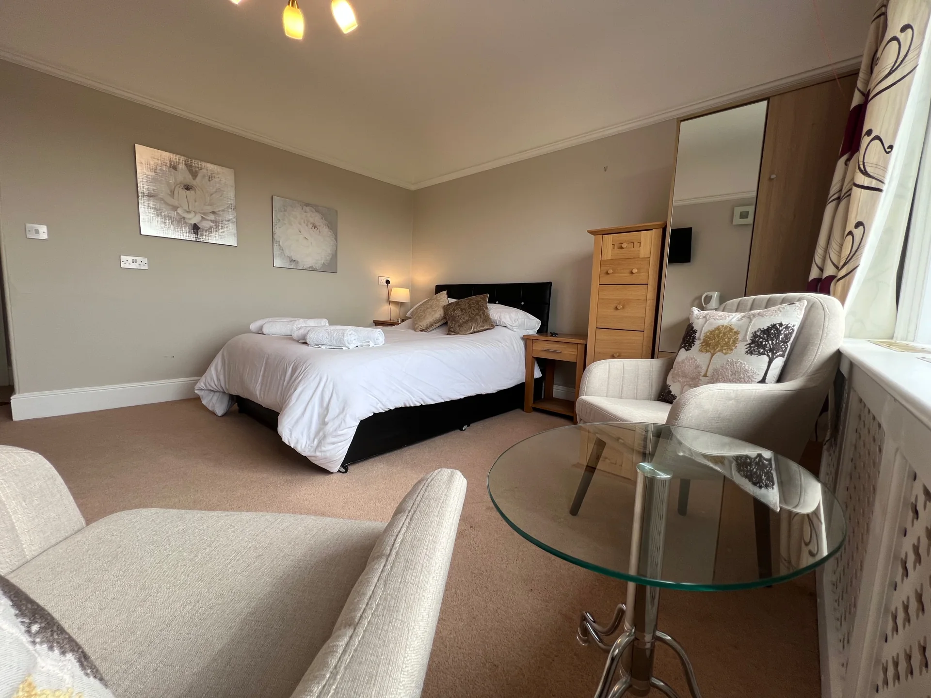 A furnished room at Armstrong House with a bed, armchair and table beside the window